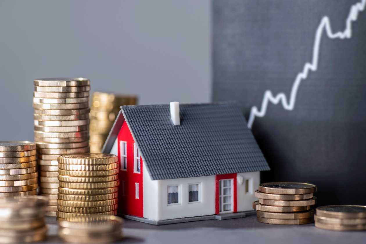 A model house beside stacks of coins and a rising chart